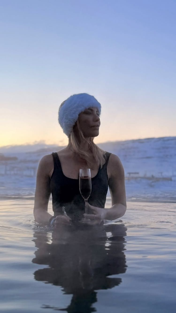 Woman in a hot spring holding champagne with snowy mountains in the background