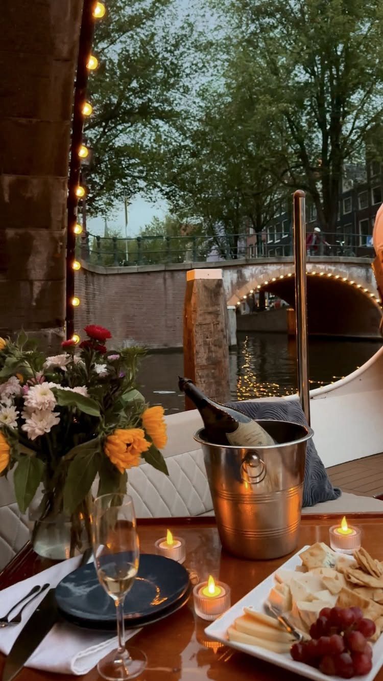 Luxury boat deck with champagne and charcuterie overlooking an Amsterdam city canal bridge.