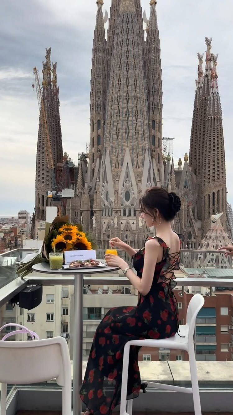 Woman in floral dress dining on a balcony overlooking the Sagrada Familia basilica.