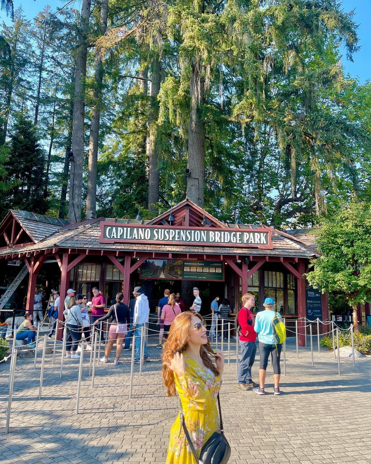 Woman in yellow dress standing before the Capilano Suspension Bridge Park entrance building.