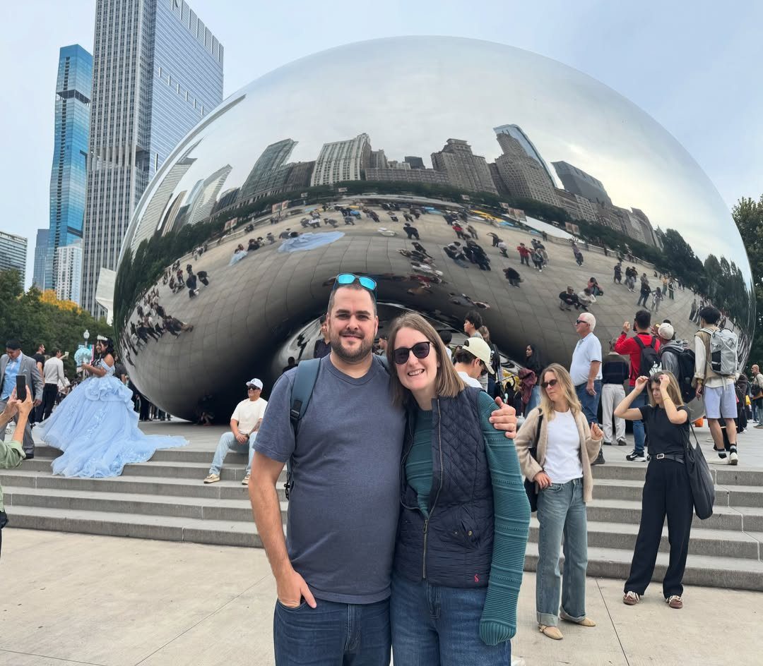 Smiling couple posing in front of the reflective Cloud Gate sculpture in Chicago.