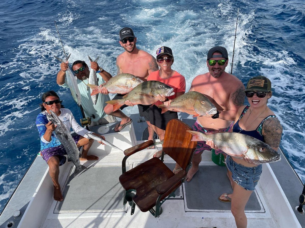 Five people on a boat holding large fish caught during a fishing trip.