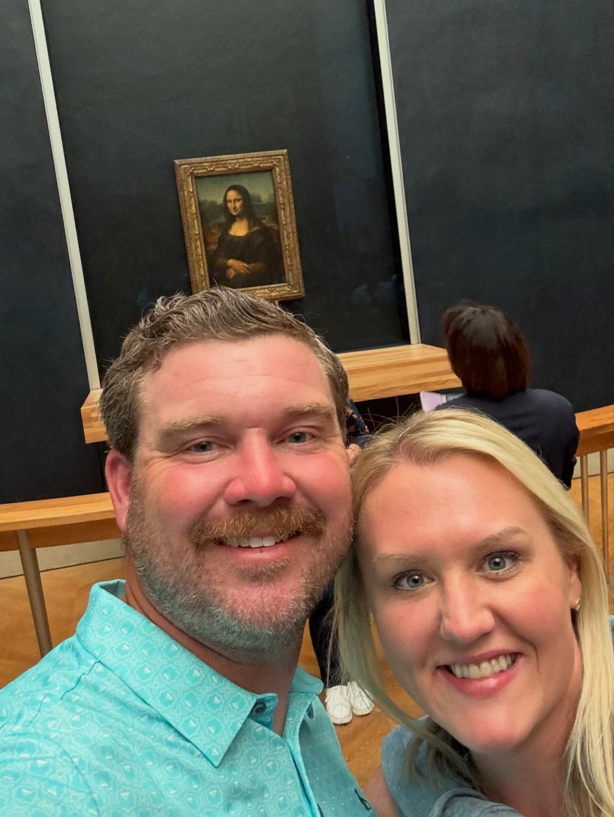 Smiling couple taking a selfie in front of the Mona Lisa painting in a museum
