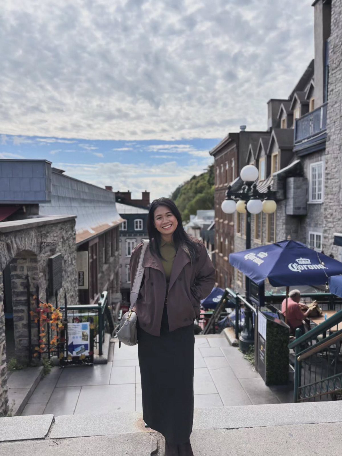 Smiling woman in a brown jacket standing on a stone street in Quebec City.
