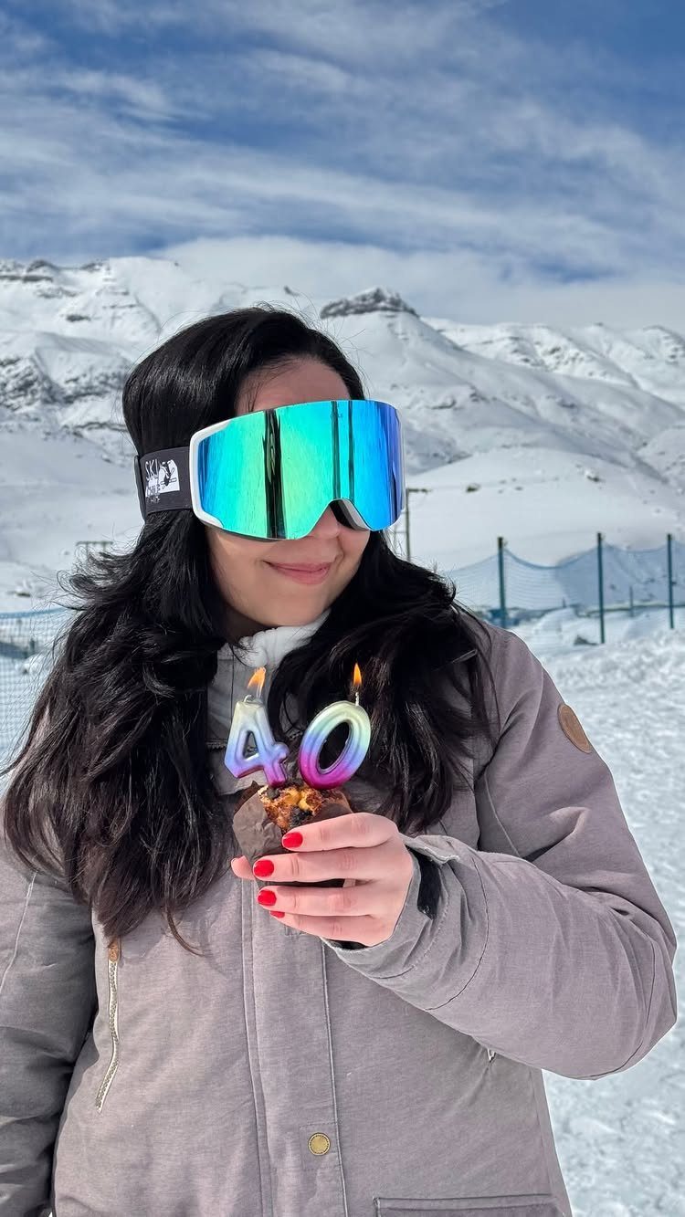 Woman in ski gear holding a birthday cake with 40 candles in snowy mountains