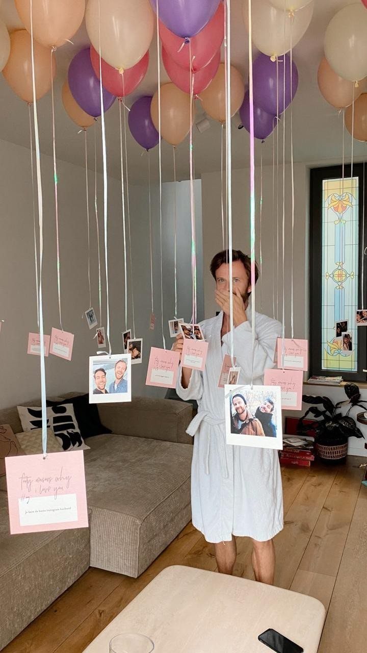 Woman in white robe surrounded by balloons with hanging photos and birthday cards.