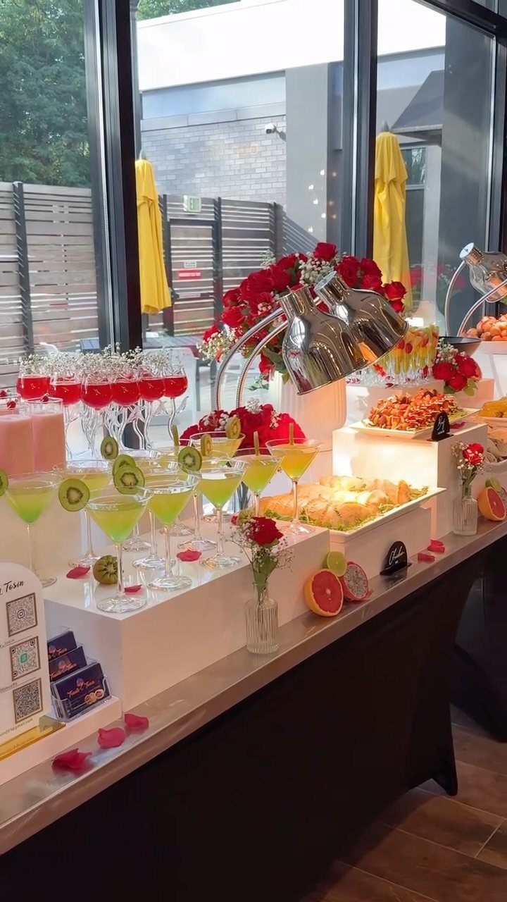 Colorful cocktails and fruit platters arranged on a white buffet table with red roses.