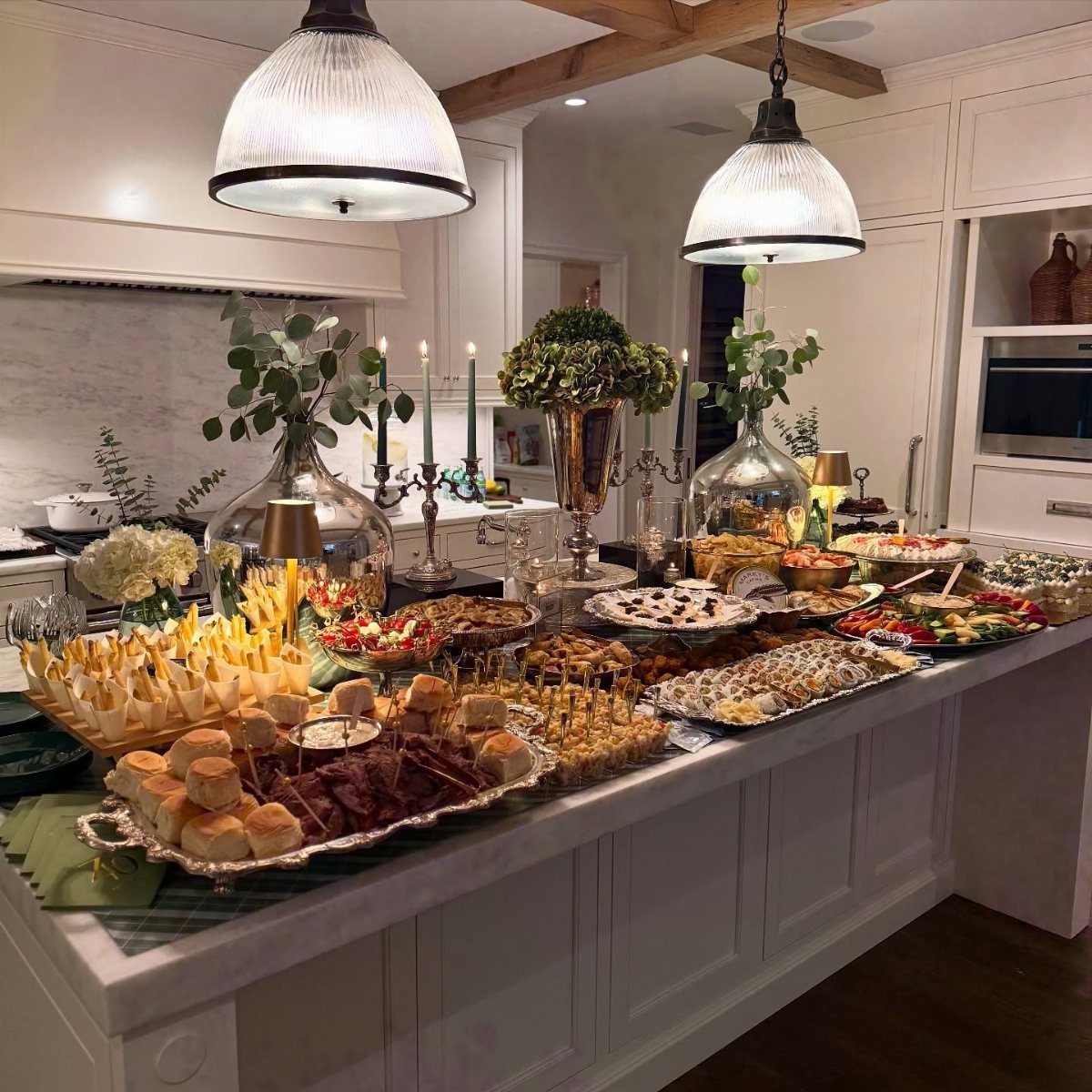 Lavish appetizer spread on a white kitchen island with candles and greenery.