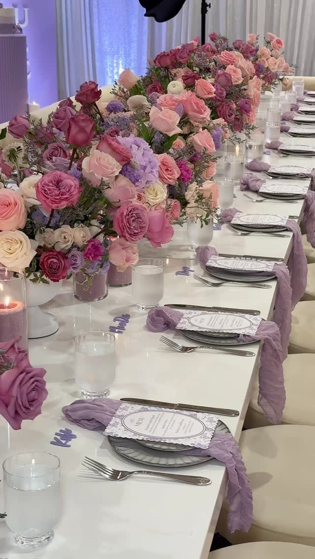 Formal dining table with a long runner of pink and purple roses and place settings.