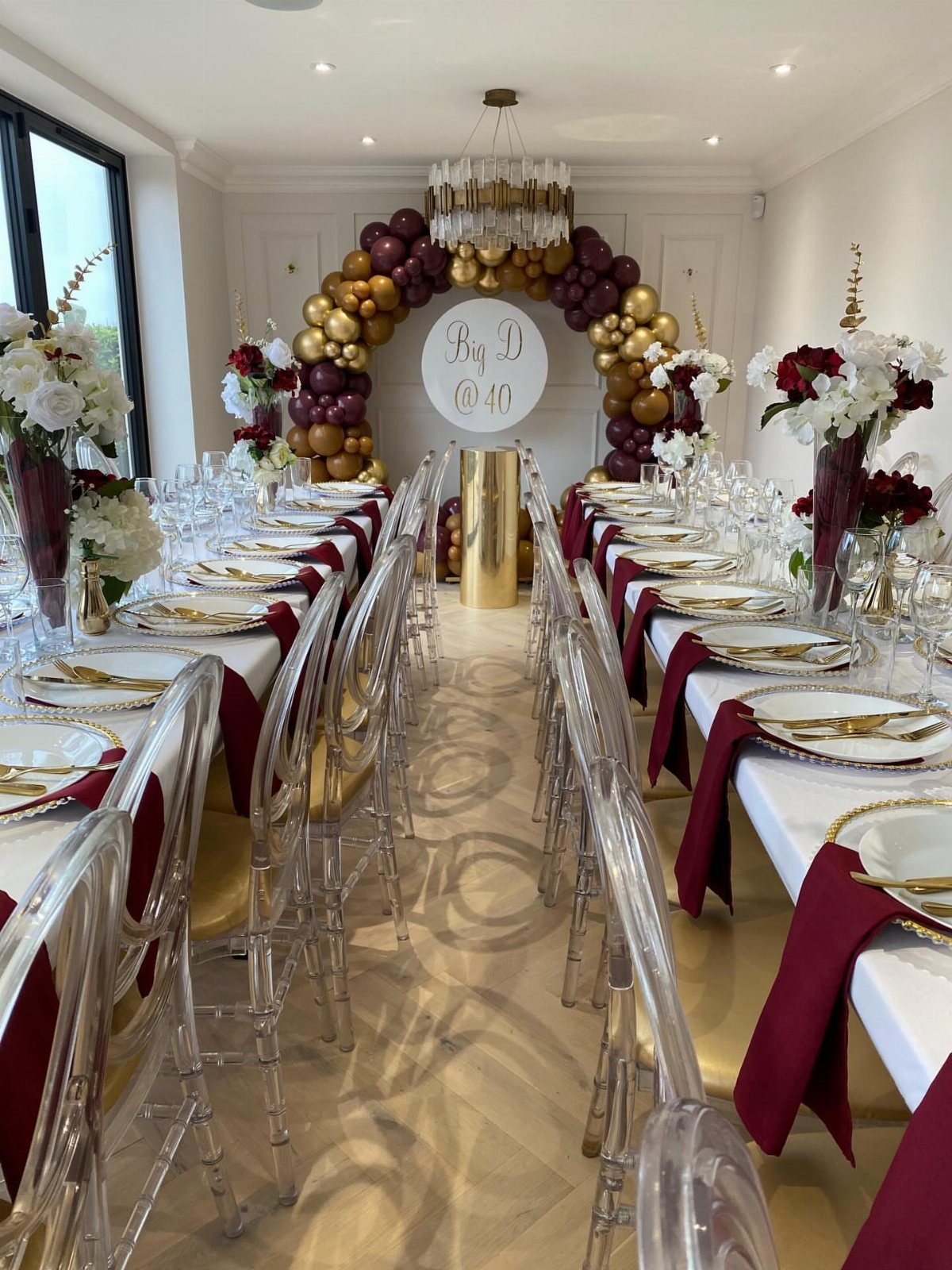 Elegant dinner table setting with burgundy accents and a 40th birthday balloon arch.