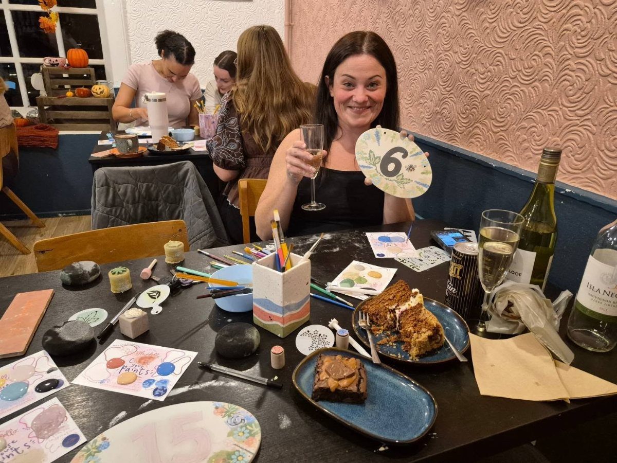 Woman holding champagne and a painting at a birthday art party table.