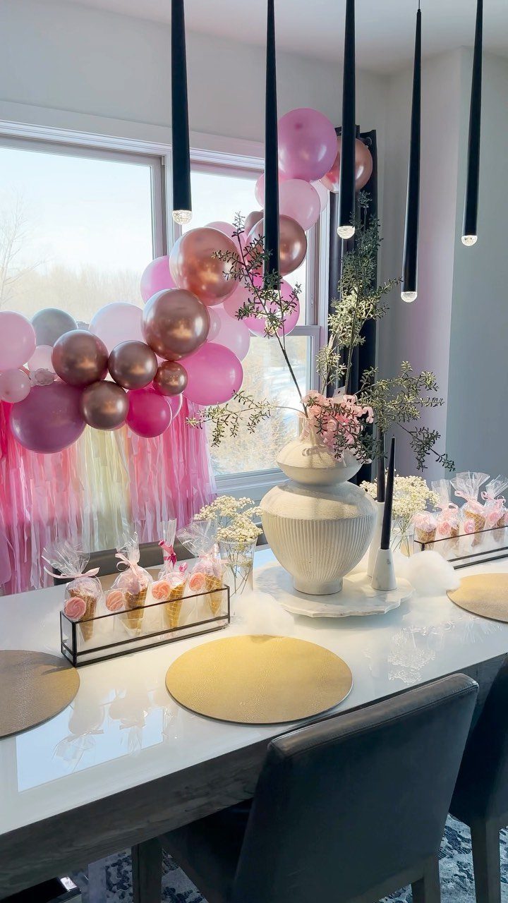 Decorated dining table with gold placemats and a pink and rose gold balloon arch.