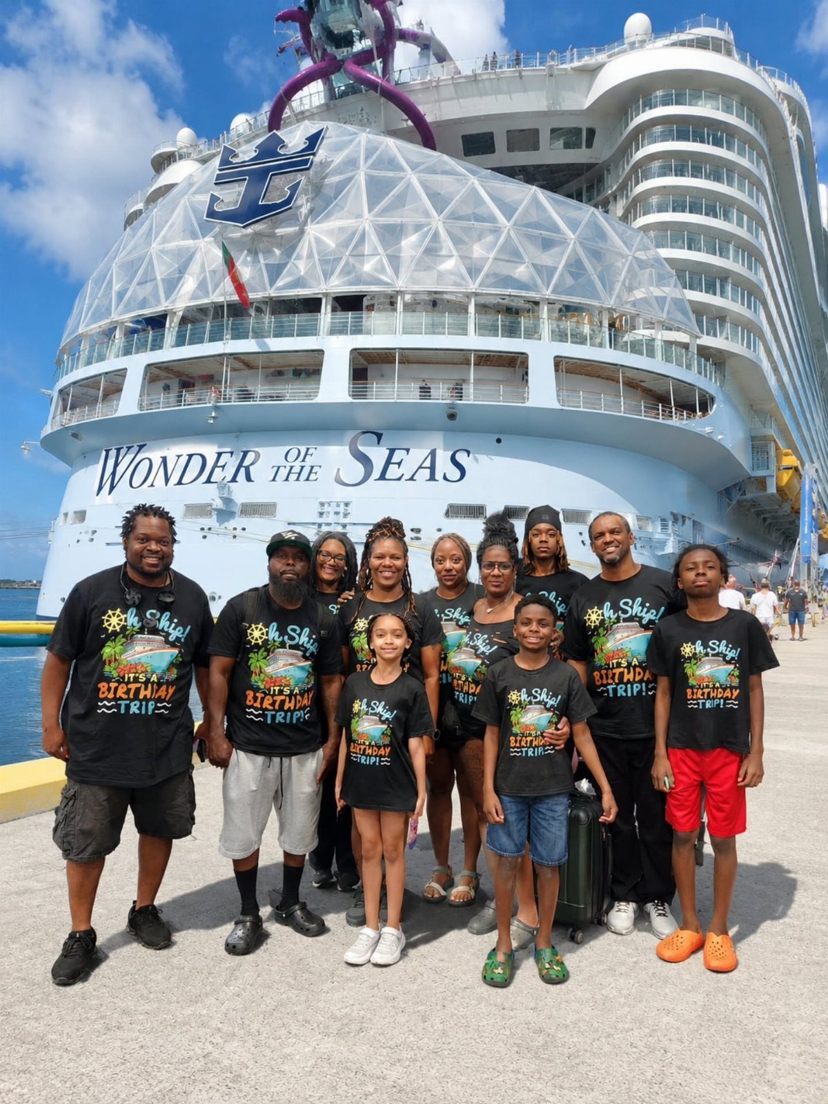Group of people in matching shirts posing before the Wonder of the Seas cruise ship.