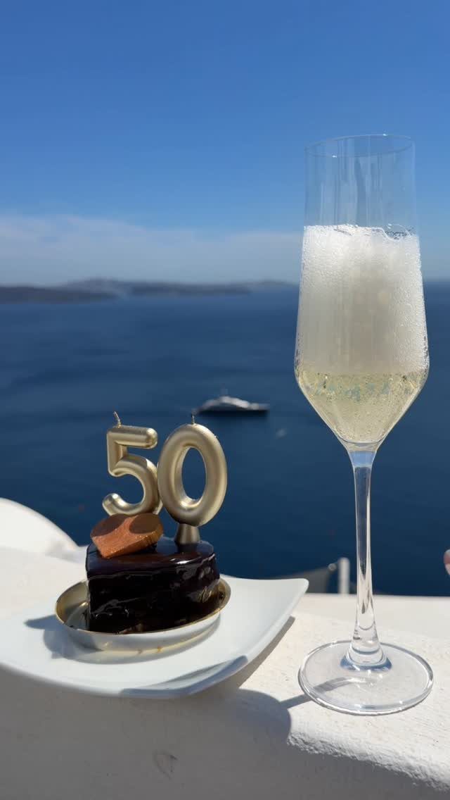 Chocolate cake with gold 50 candles and champagne overlooking a blue ocean horizon.