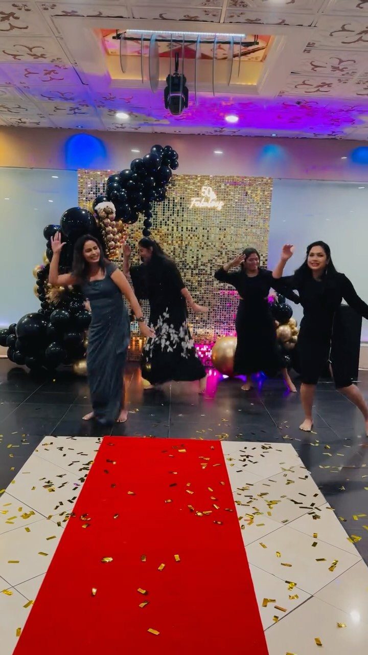 Four women dancing at a party with gold sequins and black balloons.
