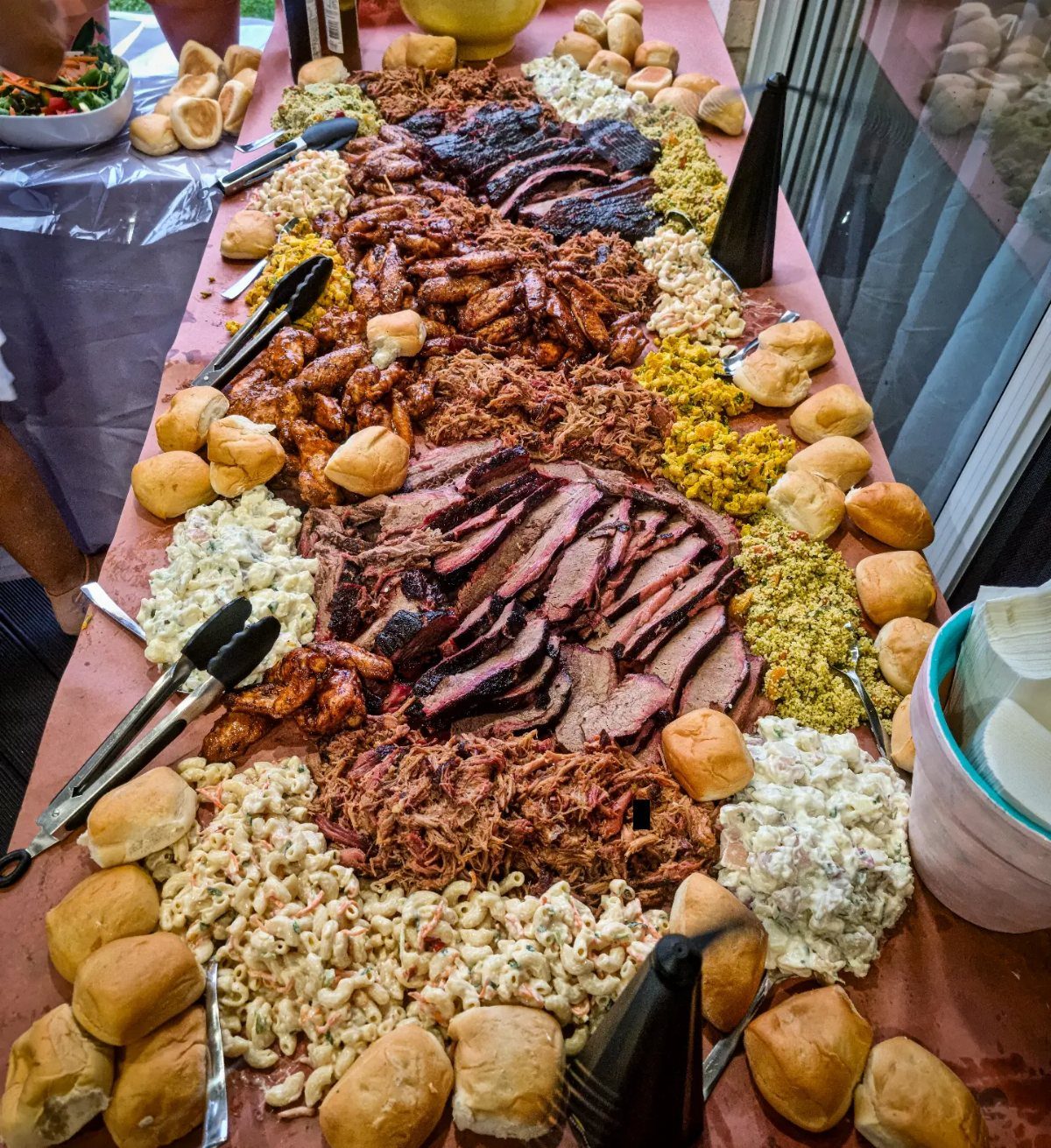 BBQ feast with sliced brisket, pulled pork, pasta salad, and dinner rolls.