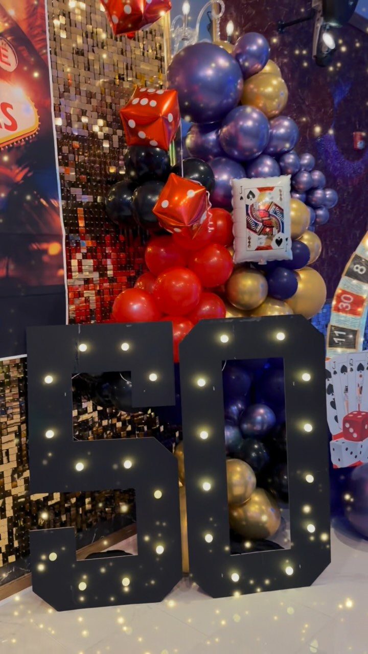 Large illuminated number 50 surrounded by casino-themed balloons, dice, and playing cards.