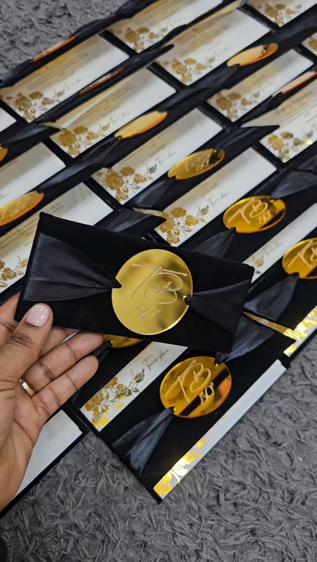 Black velvet invitations with gold seals and ribbons arranged on a grey surface.