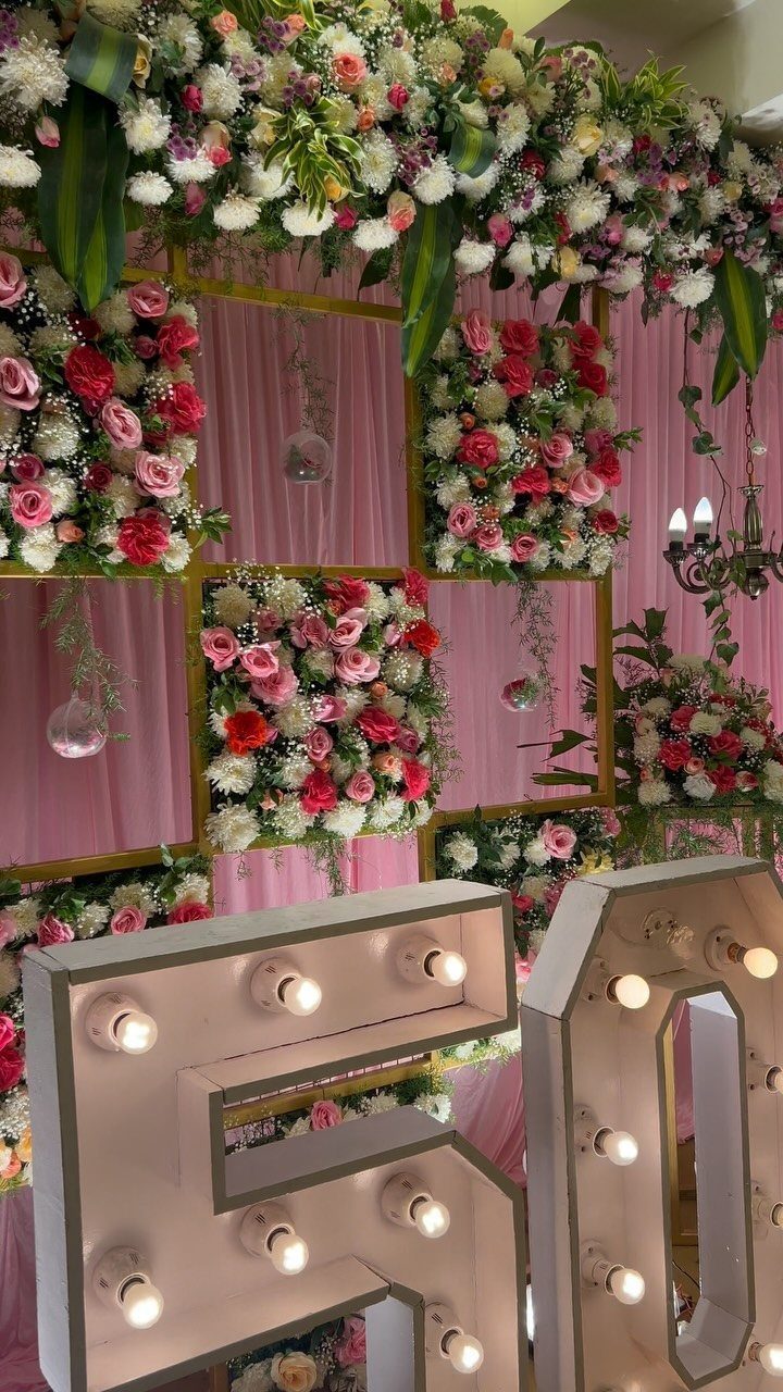 Illuminated number 50 in front of a floral gold grid backdrop with pink curtains