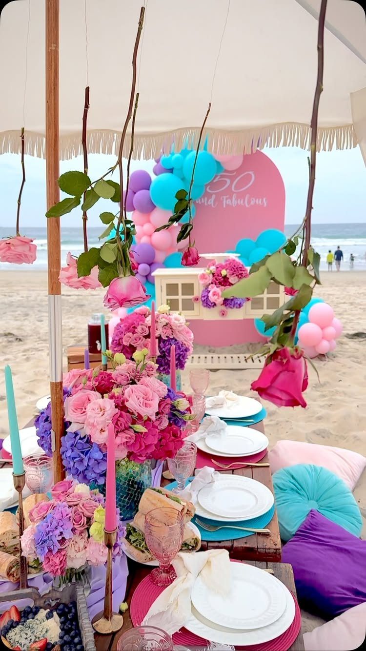 Lavish beach picnic setup with pink flowers, balloons, and 50th birthday decorations.
