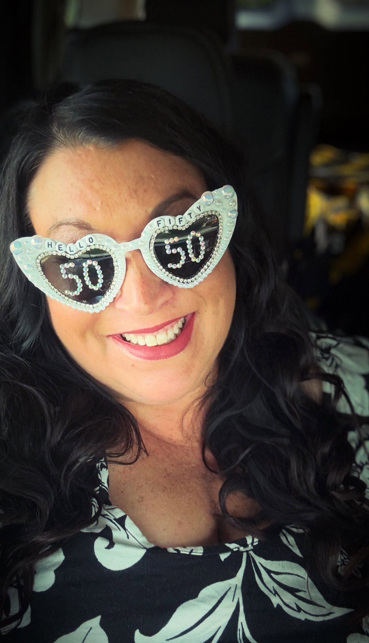 Smiling woman wearing heart-shaped glittery glasses with the number 50 on them.