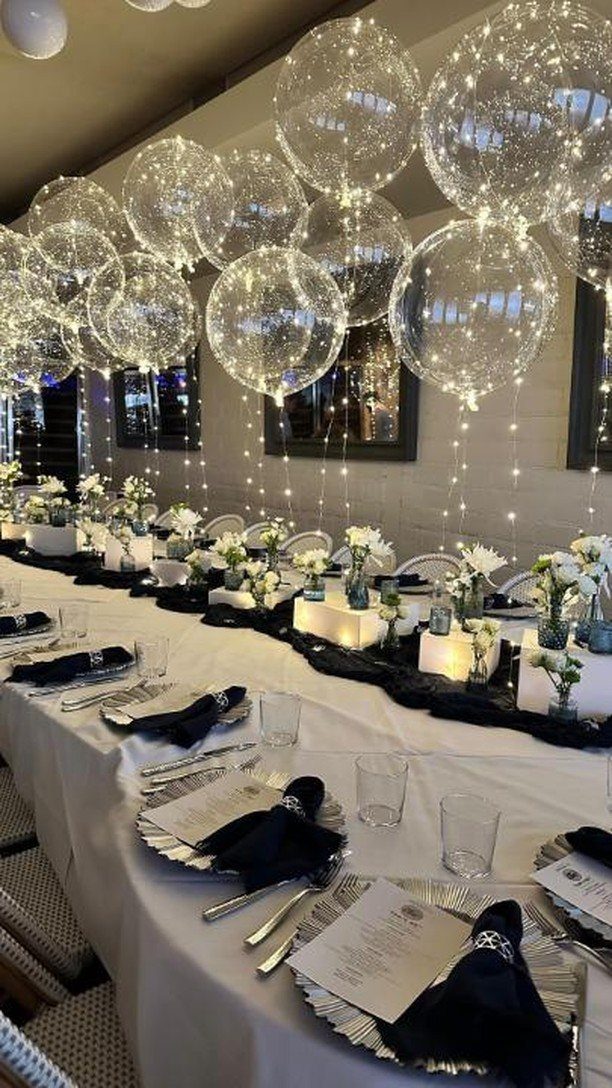 Elegant dinner table setting with white flowers and clear fairy light balloons above.