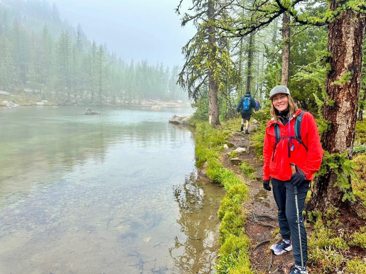 Woman in red hiking jacket standing by a foggy lake in a forest