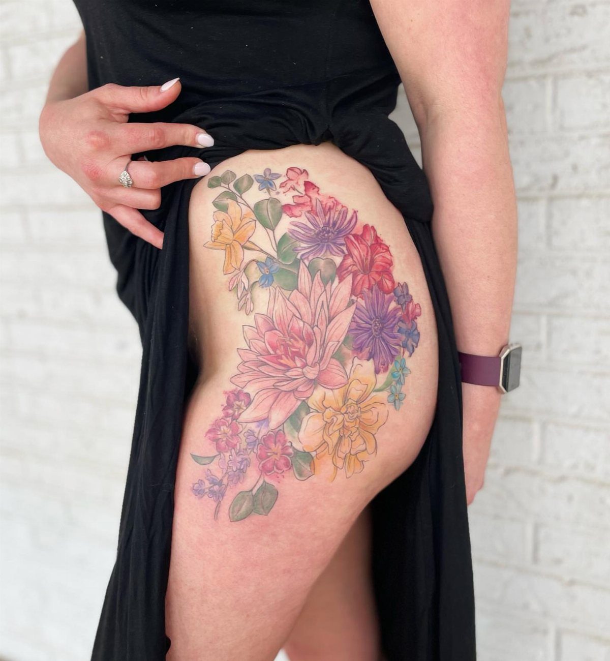 Colorful floral tattoo on a thigh featuring pink, purple, and yellow blossoms.