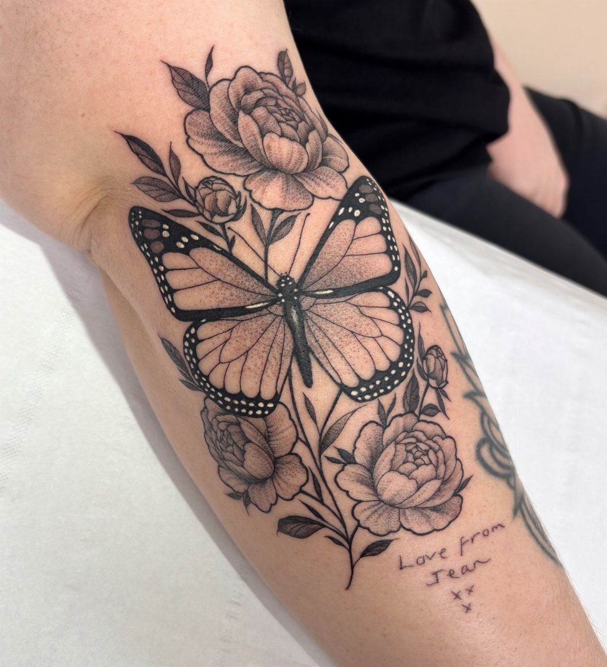 Butterfly and peony tattoo in black and grey ink on a forearm