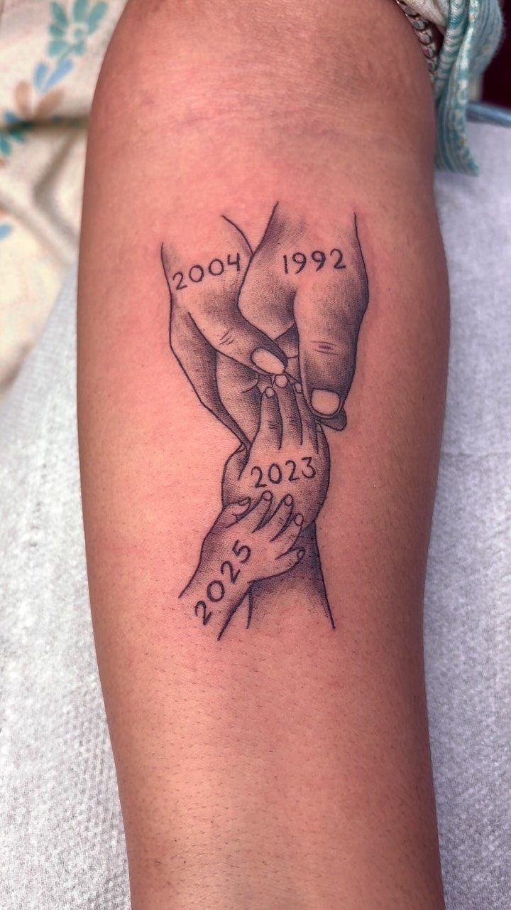 Black and grey tattoo of overlapping hands with various years on a forearm