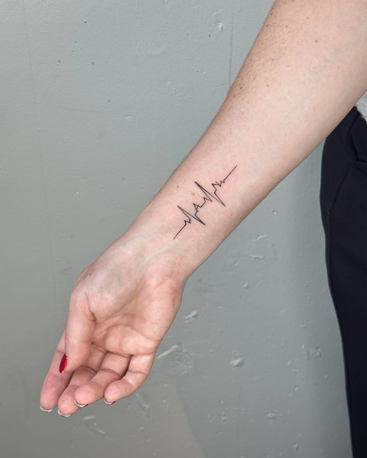 Heartbeat line tattoo on a person's inner wrist against a grey background