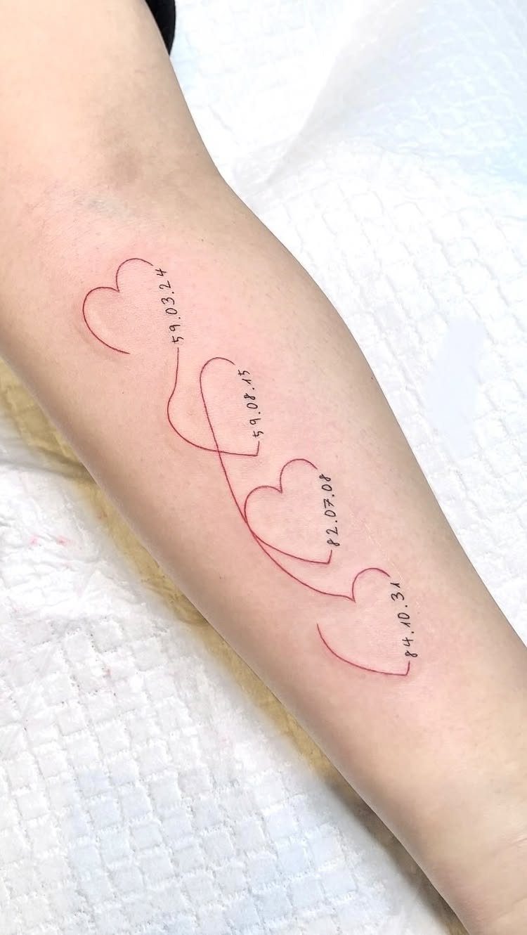 Red ink tattoo of four interlocking hearts with dates on a forearm