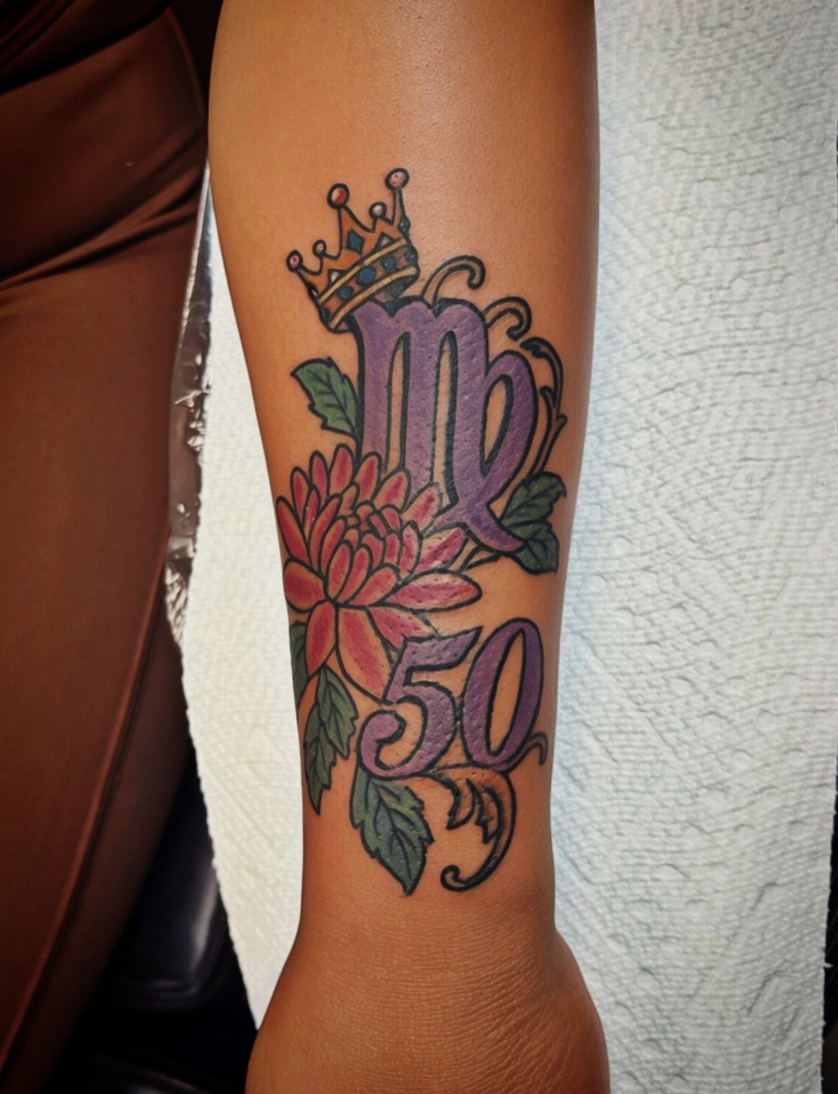 Colorful forearm tattoo featuring a Virgo symbol, red flower, and the number 50.