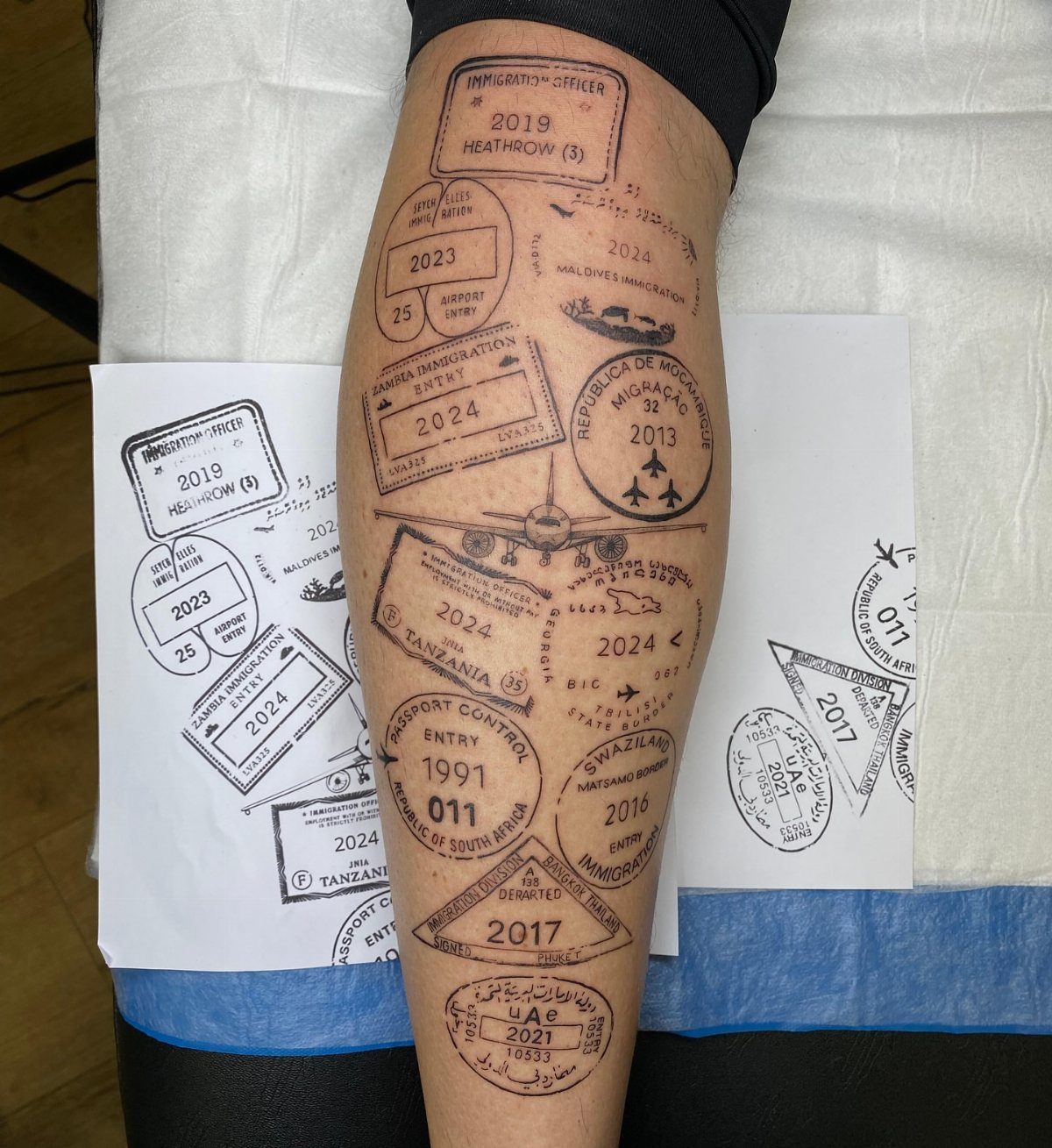 Passport stamp tattoos on a person's leg featuring travel dates and an airplane.