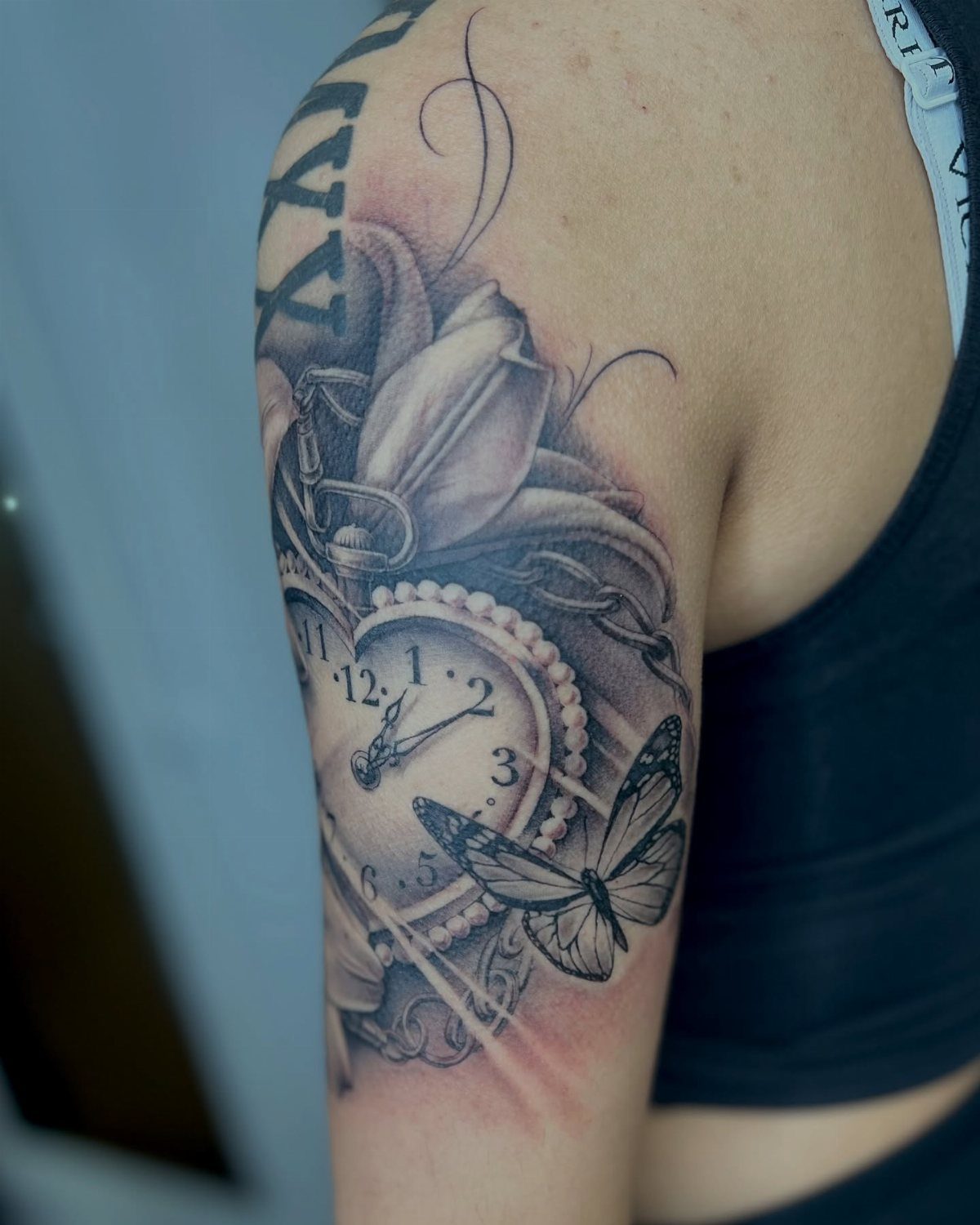 Black and grey tattoo on an arm featuring a pocket watch and butterfly.
