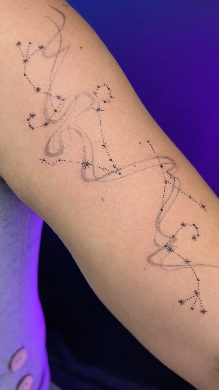 Celestial tattoo of stars and constellations with flowing lines on a person's arm.