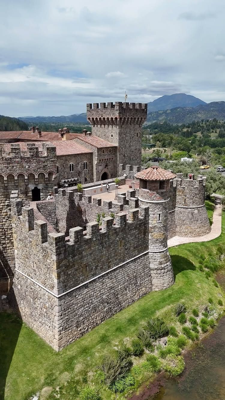 Stone castle with crenelated walls and tower overlooking a green valley and mountains