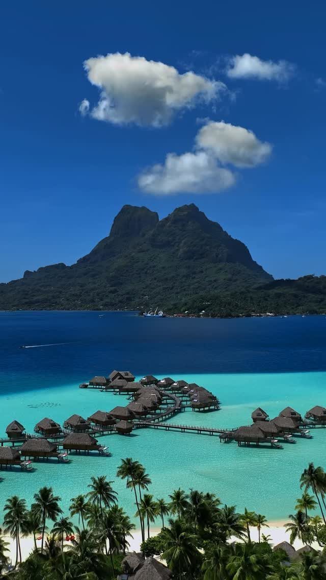 Overwater bungalows in a turquoise lagoon with a large mountain in the background.