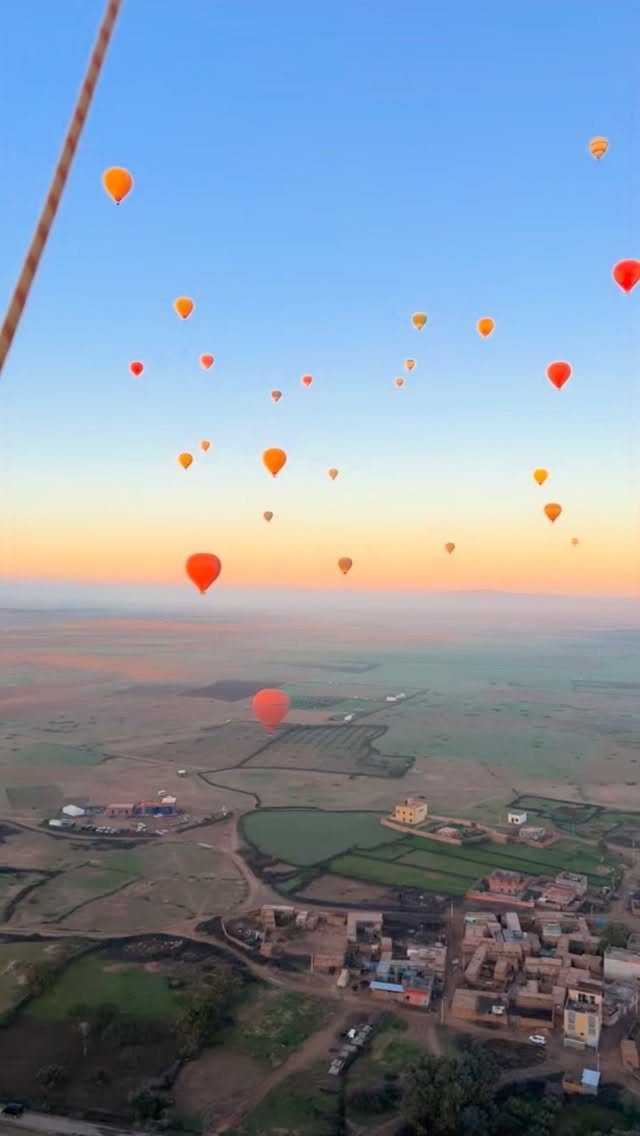 Hot air balloons floating over a rural landscape during a colorful sunrise.