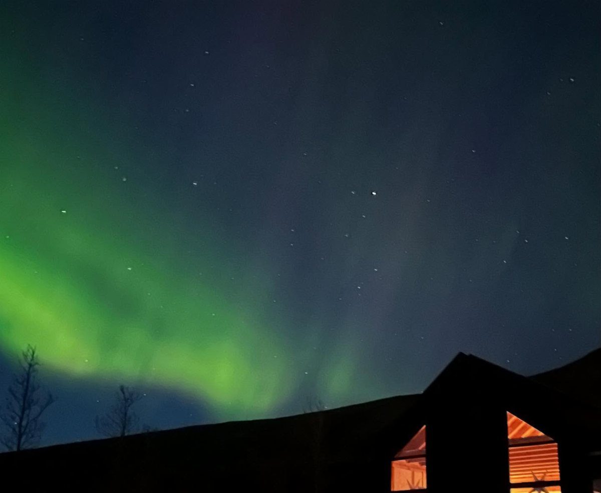 Green aurora borealis shimmering in a starry night sky above a dark house.