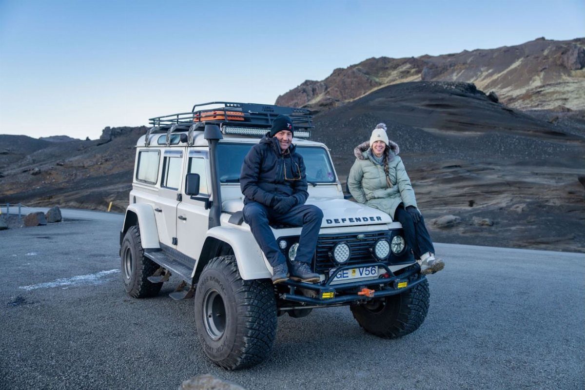 Couple sitting on a white off-road vehicle in a rocky mountain landscape.