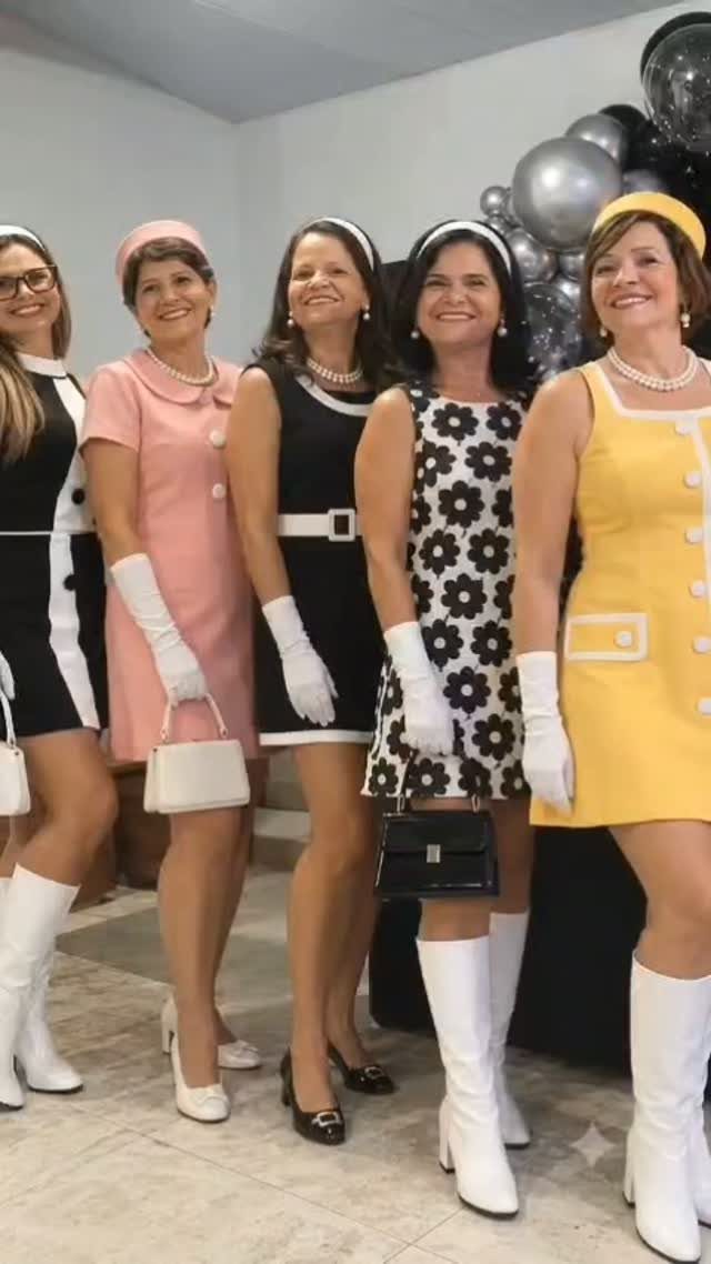Five women in colorful mod-style dresses and white gloves posing at a party.