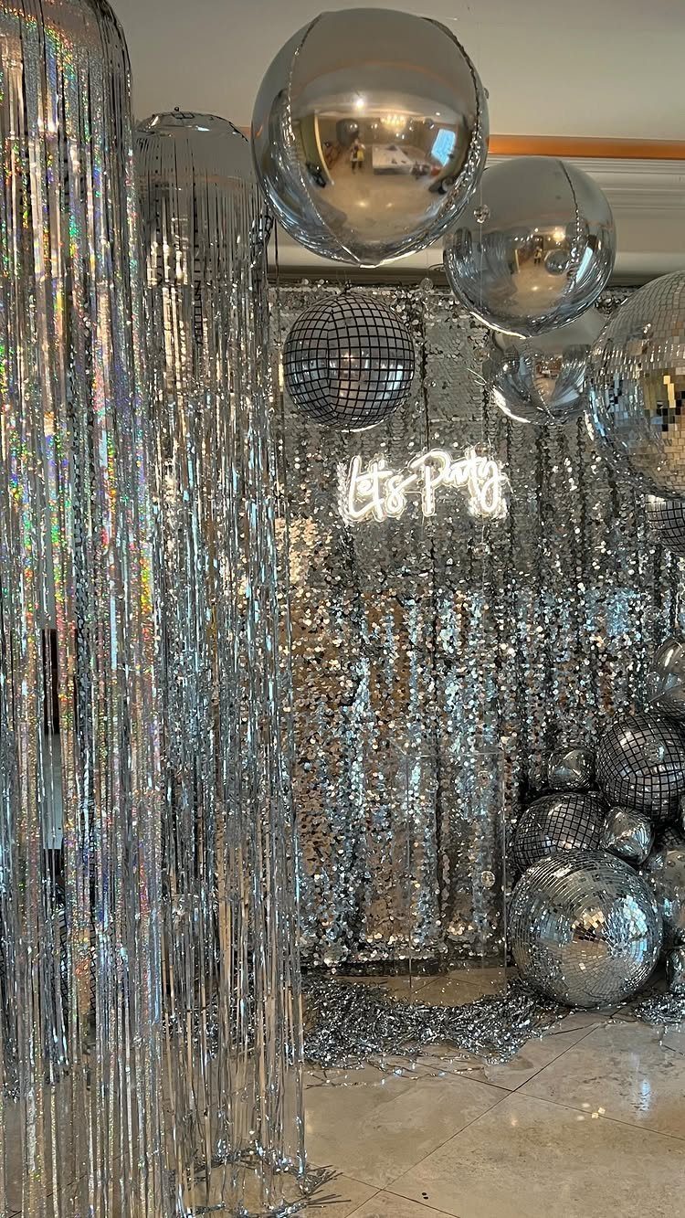 Silver party backdrop with disco balls, tinsel curtains, and a Let's Party neon sign.