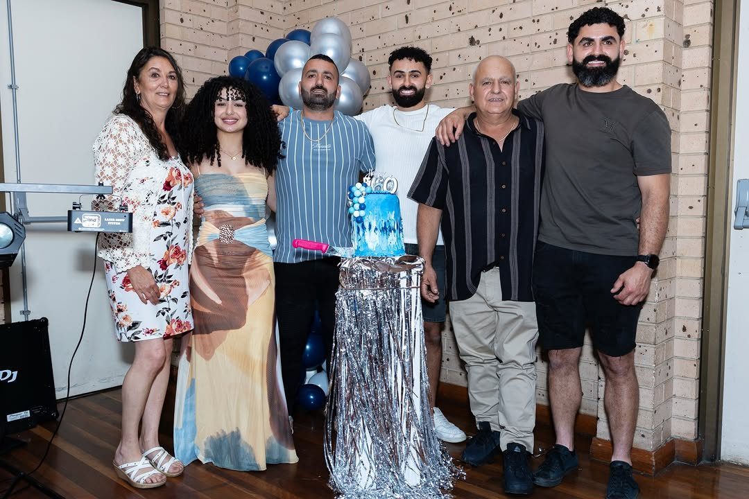 Group of family members posing around a 60th birthday cake with silver balloons.