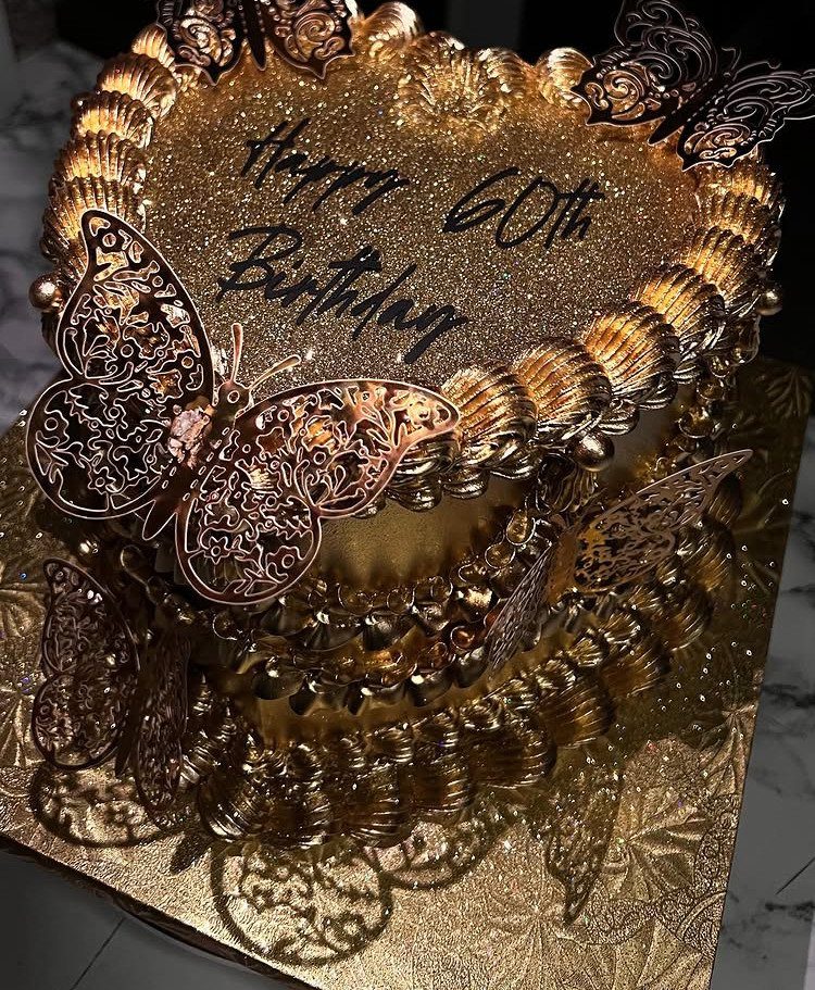 Gold glittery 60th birthday cake decorated with ornate gold butterflies and cursive writing.