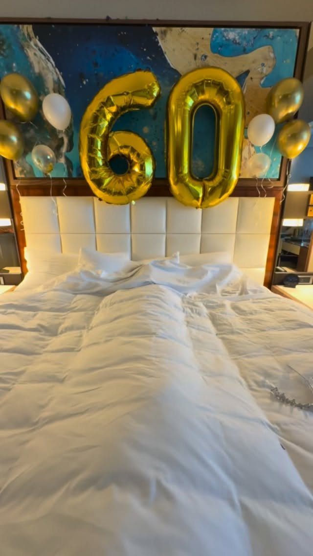 Gold number 60 balloons and white balloons decorating a bed for a birthday.