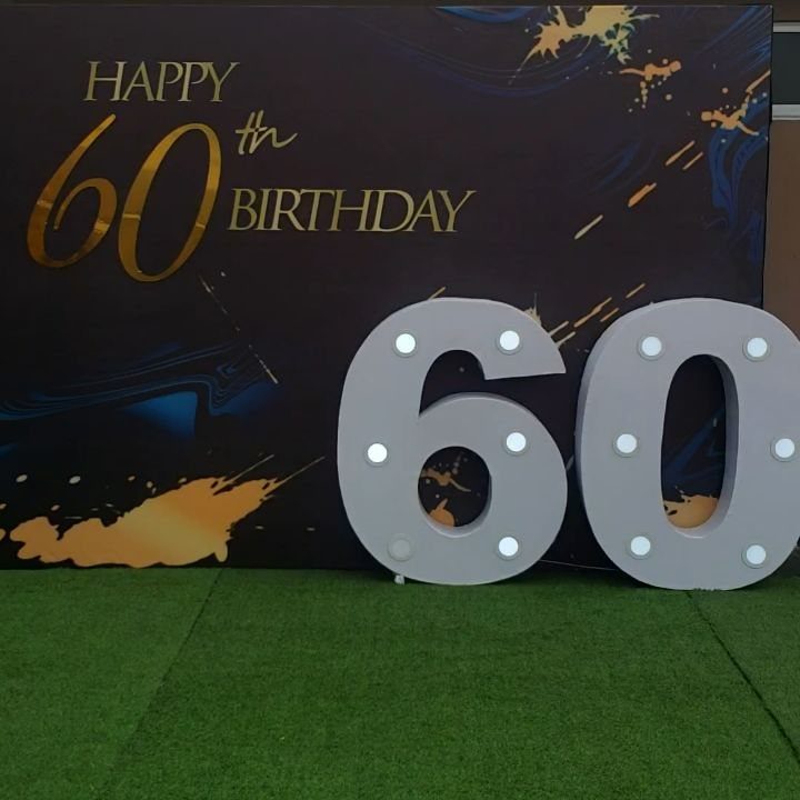 Large illuminated number 60 marquee lights in front of a birthday backdrop.