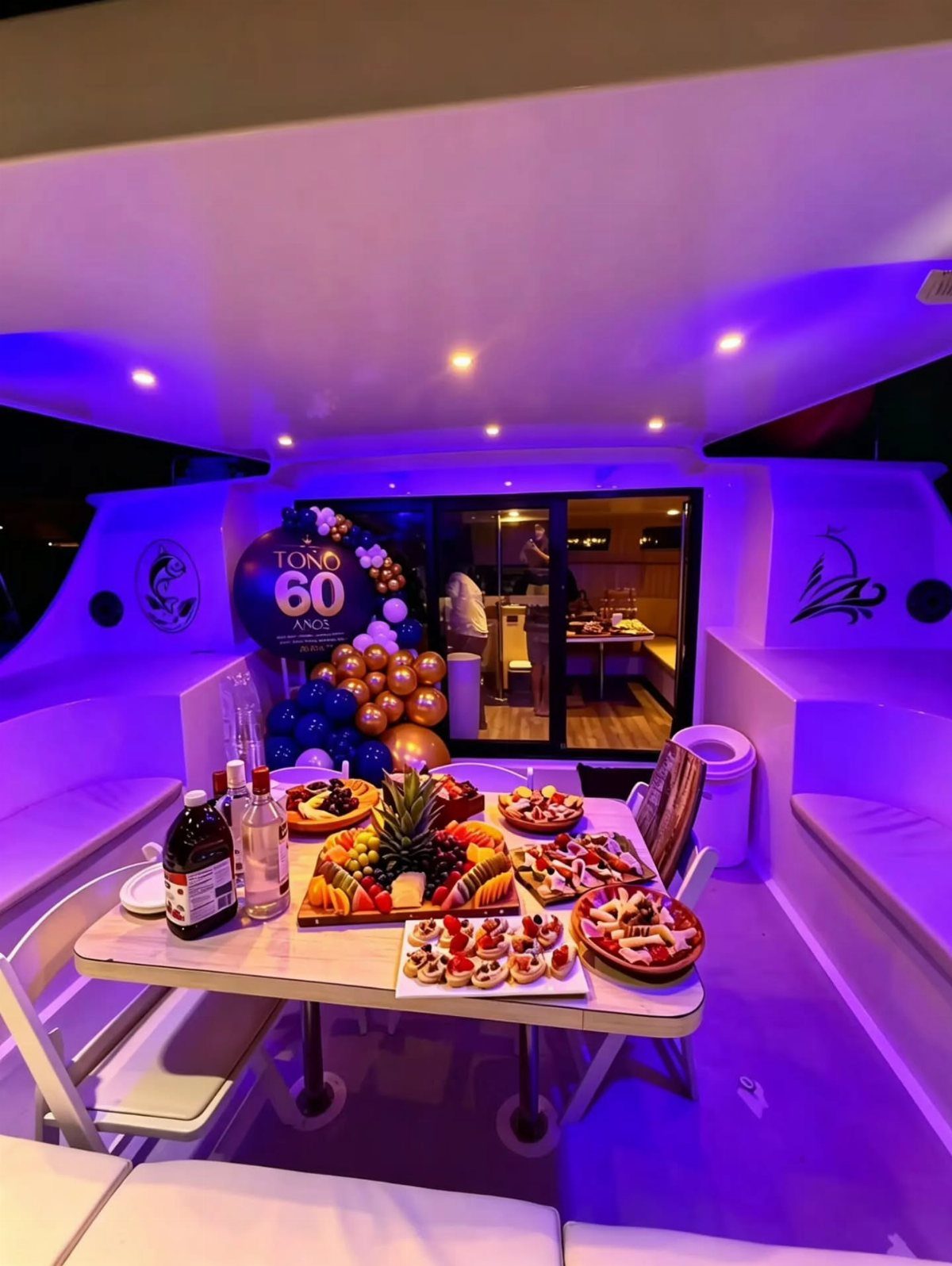 Boat cabin interior with purple lighting, food platters, and 60th birthday balloons.