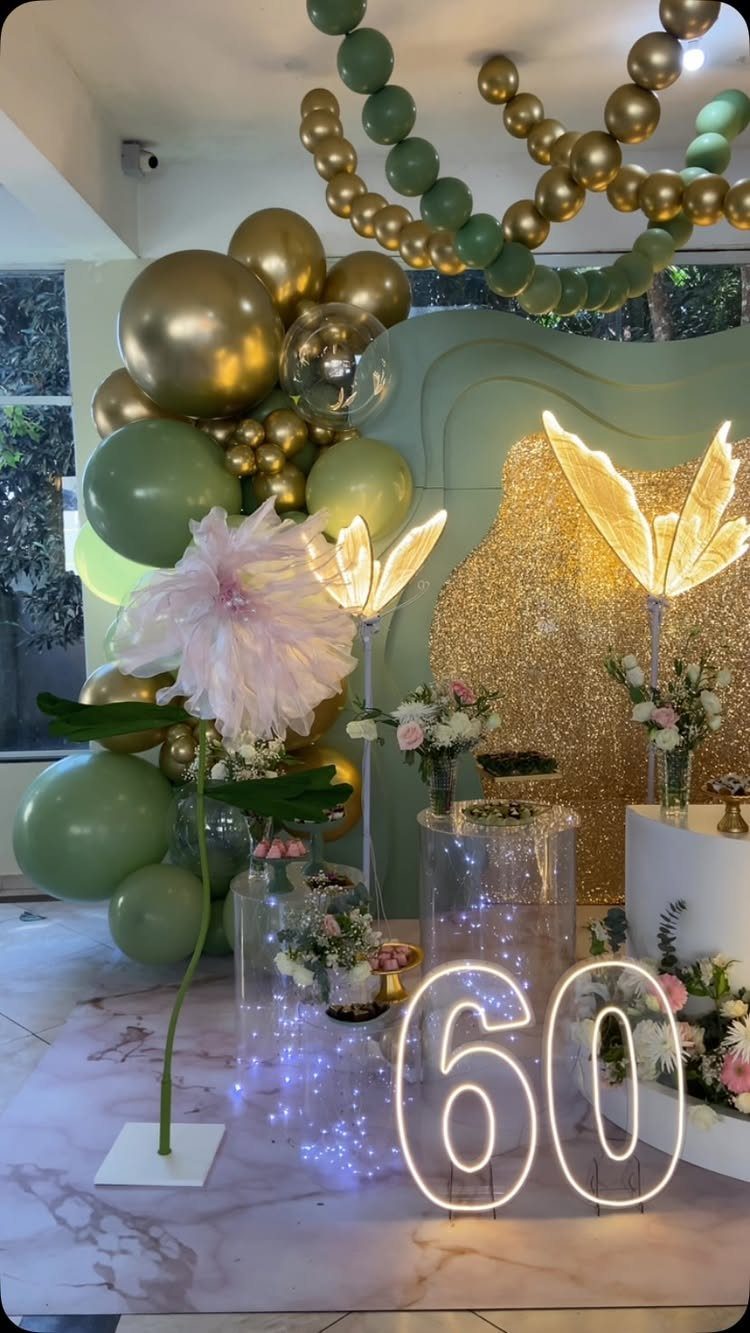 Glowing neon 60 sign with gold and green balloons and floral decorations.