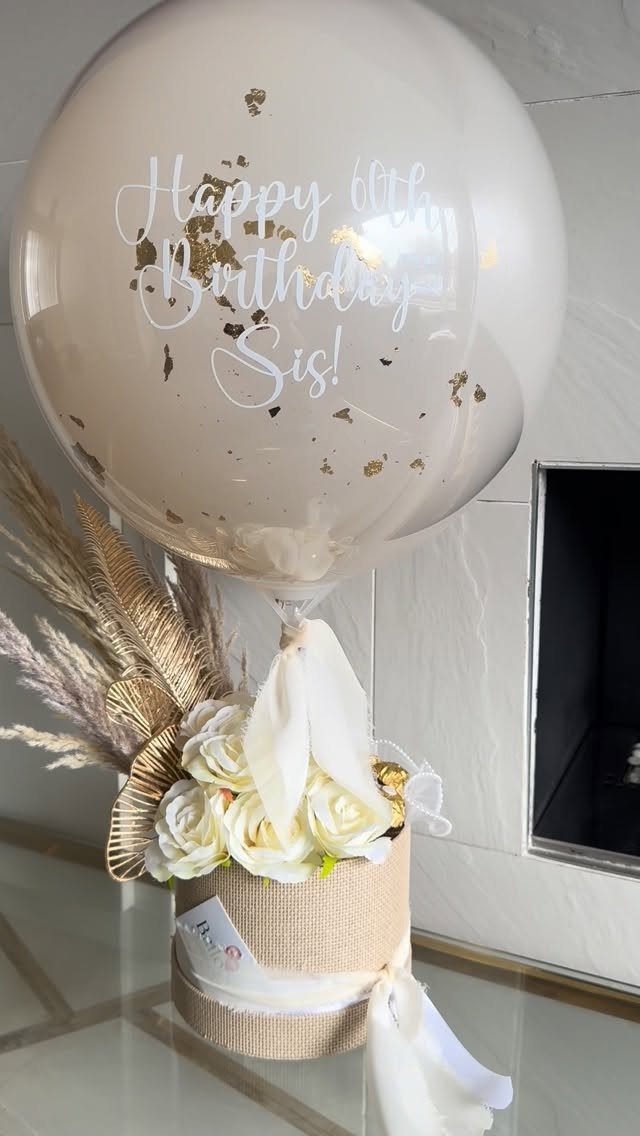 Clear balloon with 60th birthday message floating over white roses in burlap box